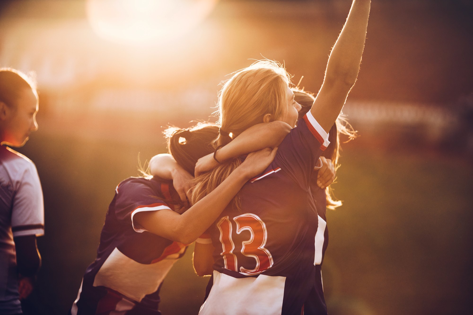 Teammates embracing in celebration on the pitch at sunset