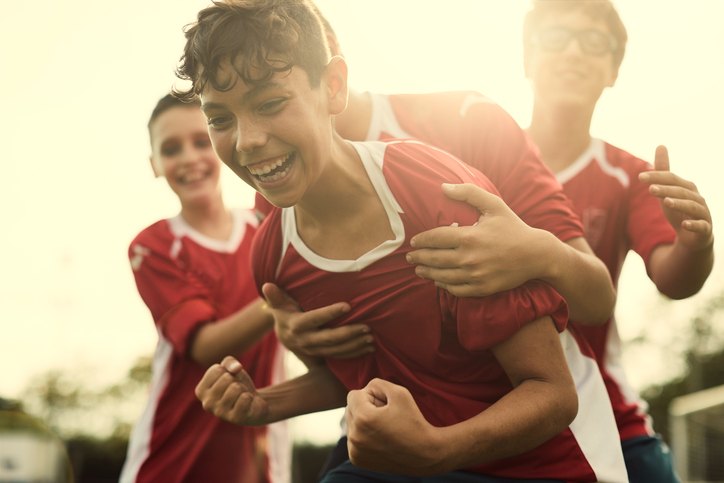 Young footballers celebrating a goal together, laughing and embracing