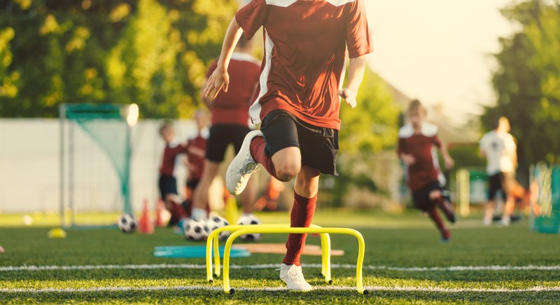 A young footballer stepping over training hurdles during a session