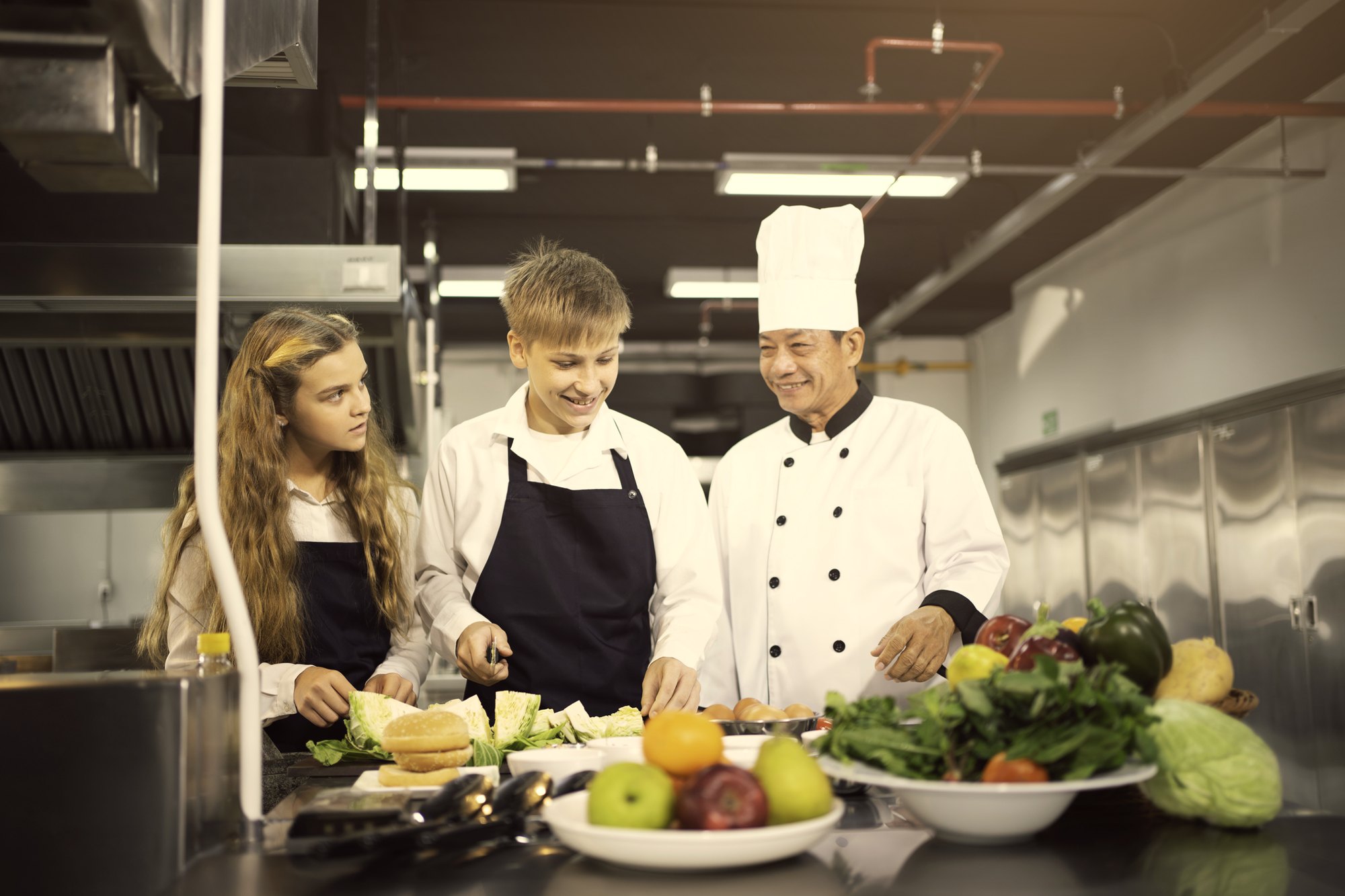 Two teenagers preparing food with a professional chef in a restaurant kitchen