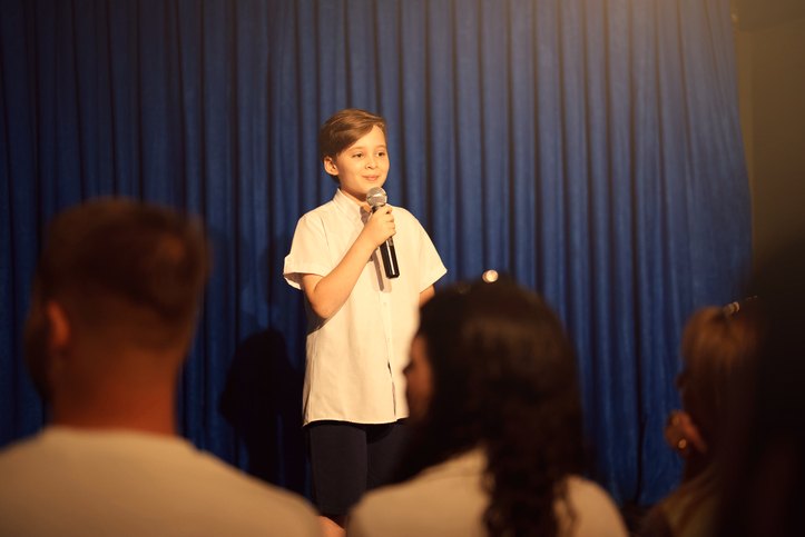 A boy speaking confidently on stage with a microphone in front of an audience